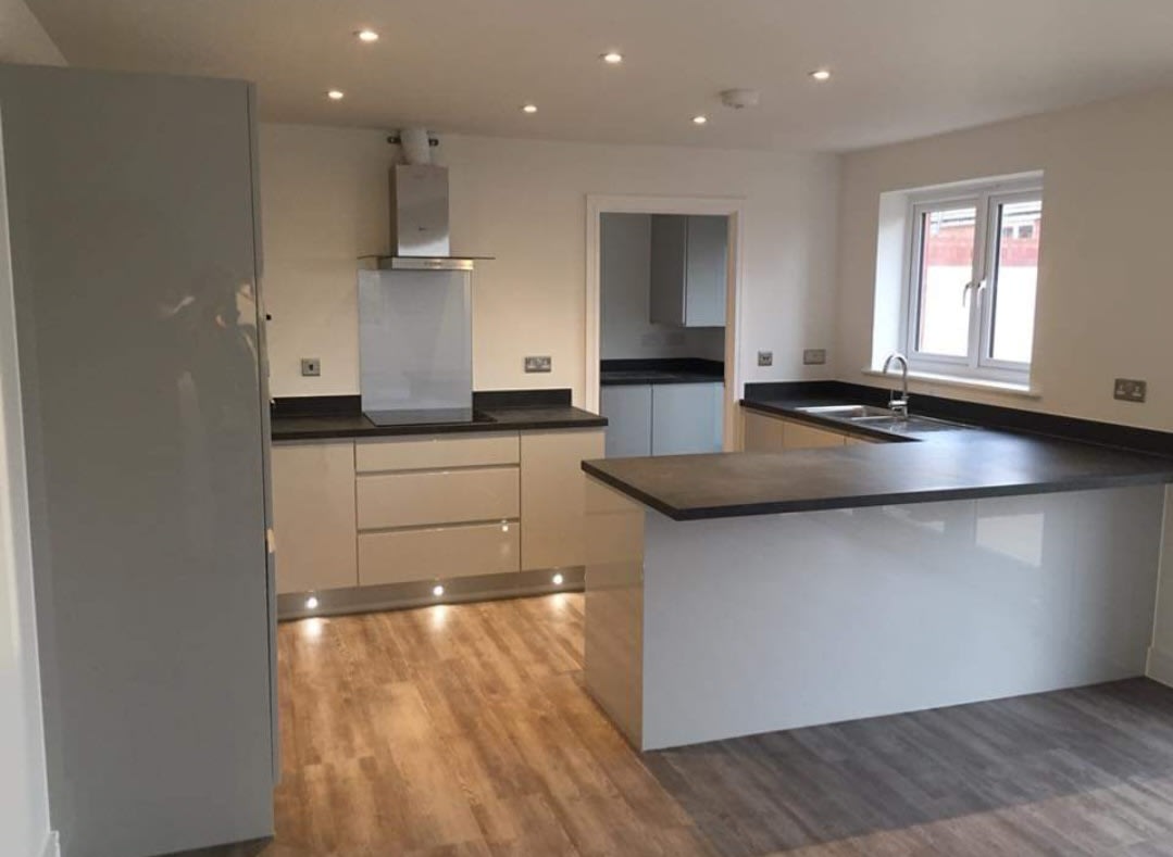 Open-plan grey gloss kitchen with a peninsula, dark worktops and plinth lighting, fitted by Tarka Kitchens