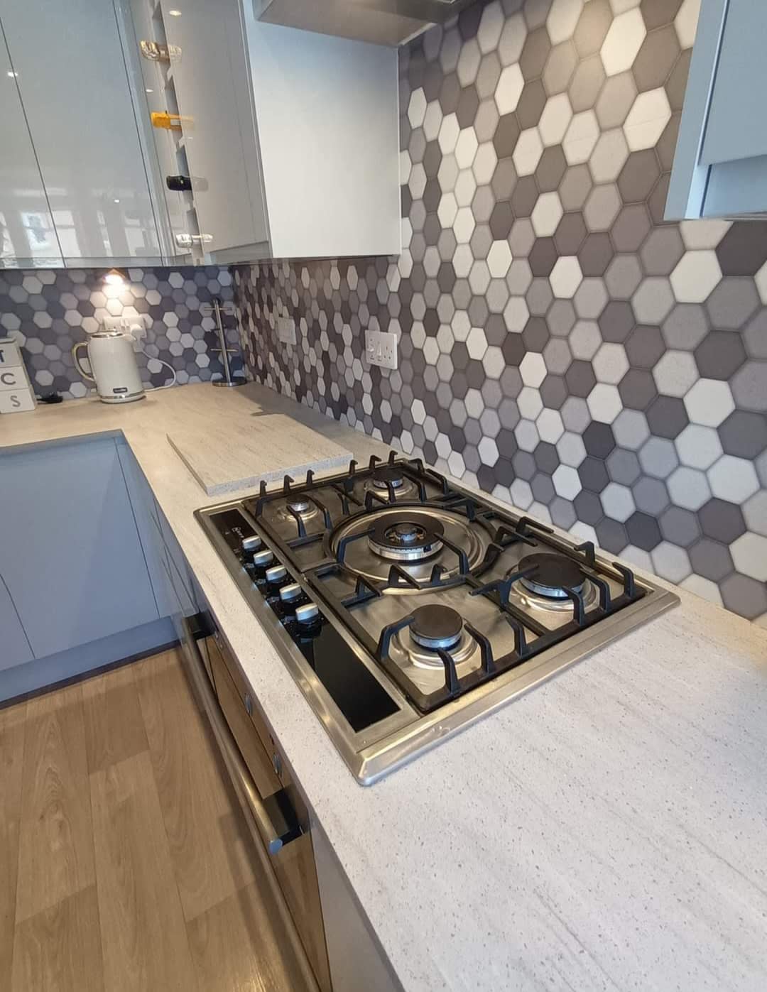Gas hob set into a stone-effect worktop with a grey hexagon tile splashback