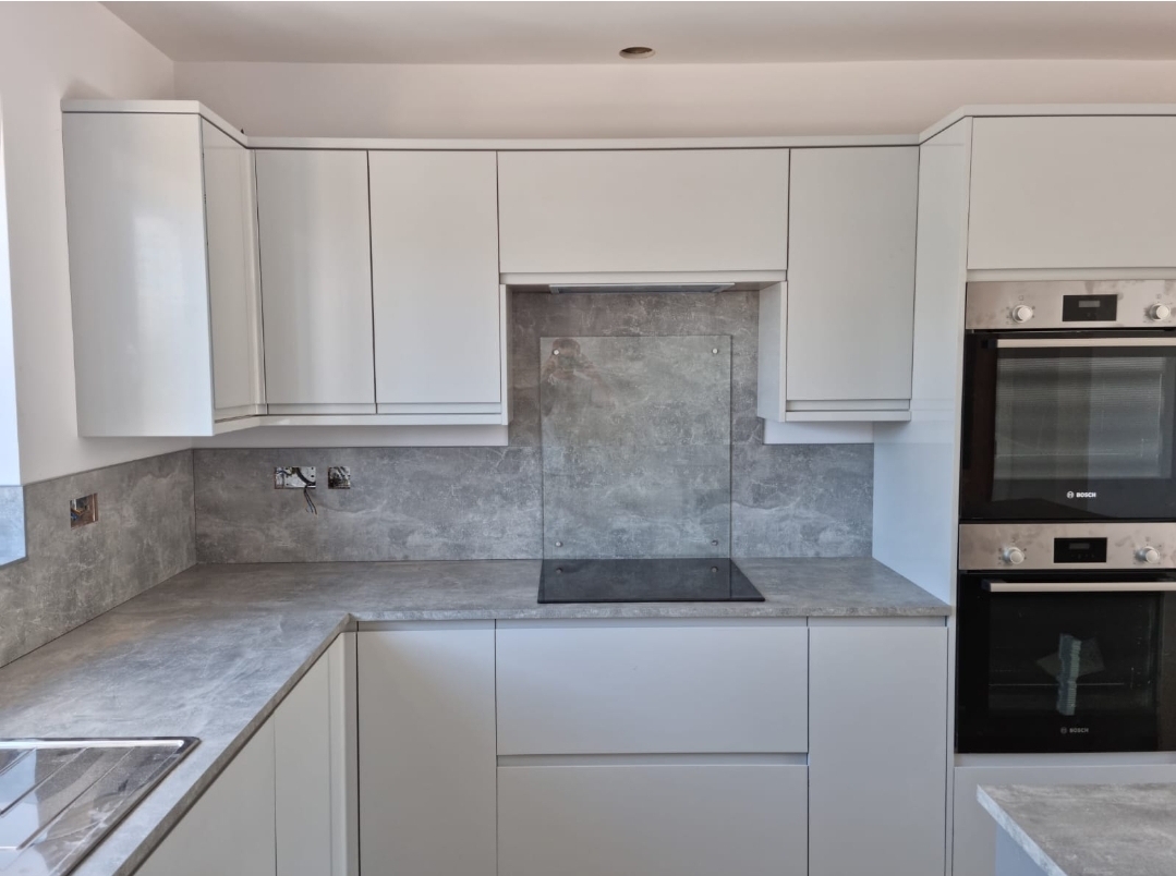 White handleless kitchen with grey marble-effect worktops and a double built-in oven